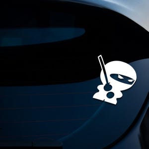 May include: White vinyl sticker of a cartoon ninja holding a sword. The ninja is wearing a mask and has a black eye.
