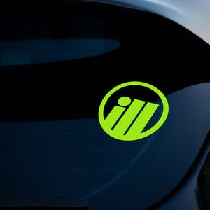 May include: A bright green sticker with a circular design. The sticker features the letters "i" and "ll" in a stylized font, enclosed within a green circle. The sticker is attached to a dark blue surface.