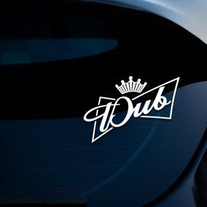 May include: White vinyl sticker with a crown and the word "Dub" in a stylised font. The sticker is on the rear window of a car.