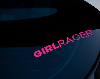 Peut inclure: Un autocollant en vinyle rose vif avec le mot "GIRLRACER" en gras, sans empattement, incliné sur une vitre de voiture. Le rose vif du texte contraste avec le fond sombre de l'intérieur et de l'extérieur du véhicule.