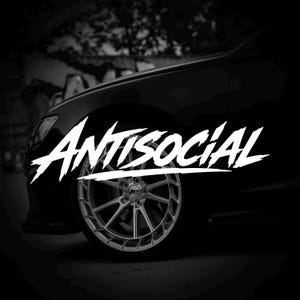 Peut inclure: Image en noir et blanc d'une roue de voiture. Le mot "Antisocial" est écrit en blanc, dans une typographie stylisée. La voiture est noire, avec un accent sur le design complexe de la roue.