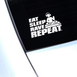 Könnte beinhalten: Weißer Vinyl-Aufkleber mit dem Text "EAT SLEEP RAVE REPEAT" und einer DJ-Grafik. Das Design zeigt eine Person mit Kopfhörern, einen Mischpult und drei Punkte. Der Aufkleber befindet sich auf schwarzem Hintergrund.