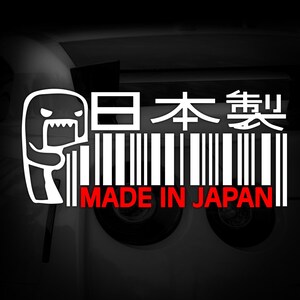 Op de afbeelding: Witte afbeelding met een stripfiguur, een barcode-ontwerp en de tekst "MADE IN JAPAN" in het rood. Japanse karakters staan boven de barcode. De achtergrond is zwart en wit.