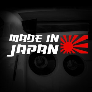 May include: A white "MADE IN JAPAN" text design with a red sunburst emblem, set against a black backdrop. The text is in a bold, sans-serif font. The image is of a car.