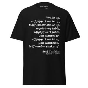 May include: Black t-shirt with white text. The text includes the phrase "wake up" and other lines of text, along with the name "Serj Tankian" and "System of a Down".