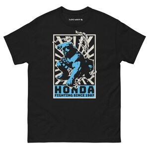 Può includere: T-shirt nera con una grafica blu di una figura di combattimento. La parola "HONDA" è in blu, con il testo "FIGHTING SINCE 1987" sotto. Il design è ambientato su uno sfondo bianco e nero con un motivo a scoppio.