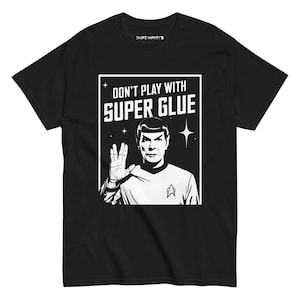 Puede incluir: Camiseta negra con un gráfico blanco de un hombre haciendo el saludo vulcano, con el texto "DON'T PLAY WITH SUPER GLUE". El diseño incluye estrellas y una insignia de Starfleet.