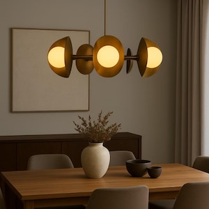May include: A modern brass chandelier with five spherical light fixtures. The light fixtures are arranged horizontally and emit a warm glow. The chandelier hangs above a wooden dining table with chairs, a vase, and bowls.