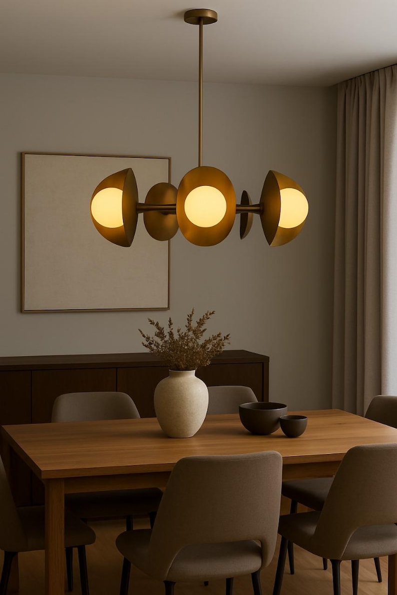 May include: A modern brass chandelier with five spherical light fixtures. The light fixtures are arranged horizontally and emit a warm glow. The chandelier hangs above a wooden dining table with chairs, a vase, and bowls.