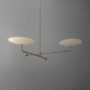 Puede incluir: Una lámpara de araña moderna y minimalista con acabado bronce. Cuenta con dos pantallas en forma de disco blanco roto suspendidas de una varilla central y brazos horizontales. El diseño incluye pequeños acentos esféricos.