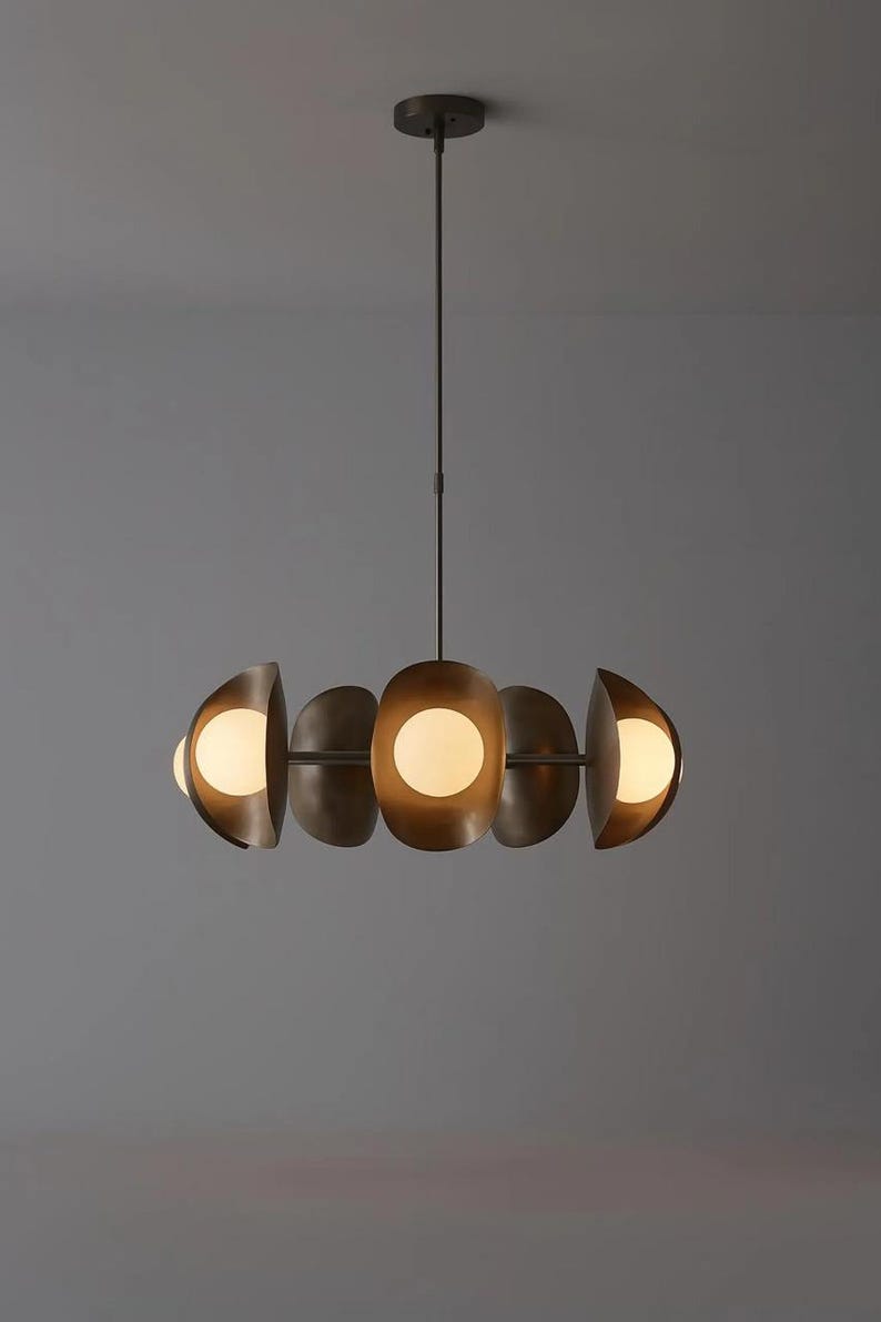 May include: A modern, bronze-toned chandelier with five semi-circular shades, each housing a spherical, glowing light. The fixture hangs from a single rod, creating a balanced and elegant lighting design. The overall aesthetic is contemporary.
