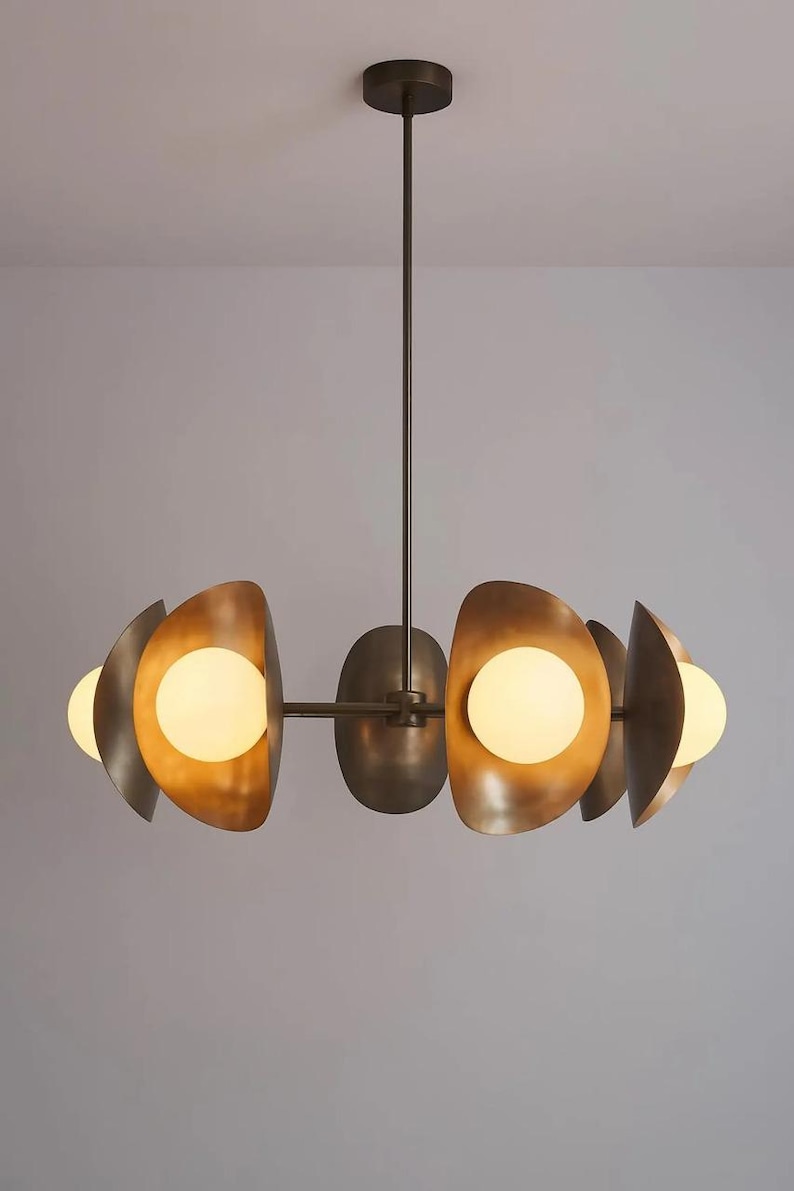 May include: A modern chandelier with a bronze finish. The light fixture features a central stem with a series of curved, metallic shades, each housing a spherical light bulb. The design is symmetrical and contemporary, suitable for interior lighting.