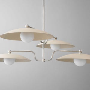 May include: A modern chandelier with a silver finish and four cream-colored, saucer-shaped shades. Each shade has a white globe light. The fixture is suspended from a central rod.