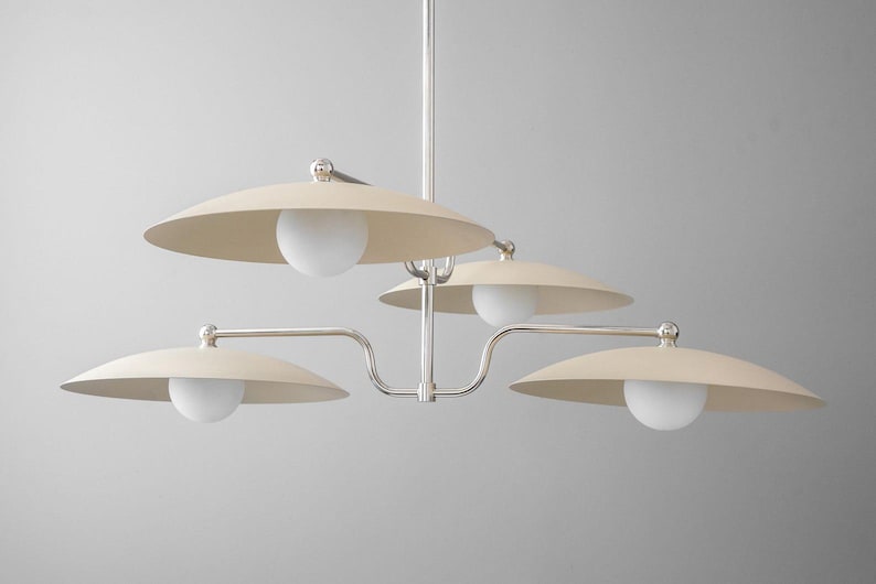 May include: A modern chandelier with a silver finish and four cream-colored, saucer-shaped shades. Each shade has a white globe light. The fixture is suspended from a central rod.