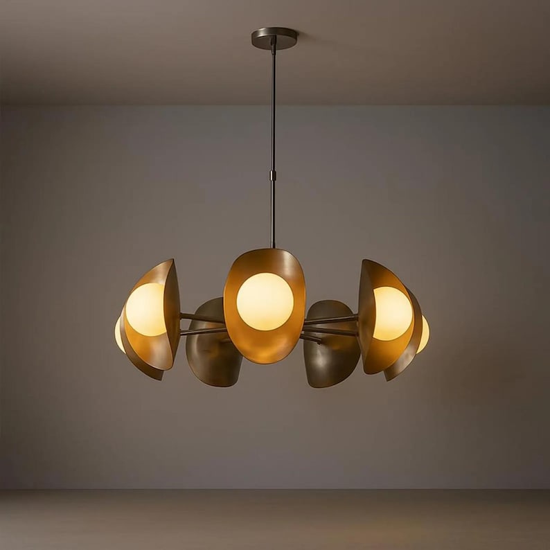 May include: A modern chandelier with a bronze finish. The light fixture has a central oval-shaped element and several curved, petal-like shades, each housing a spherical, warm-toned light. The design is sleek and contemporary, suitable for various interior styles.