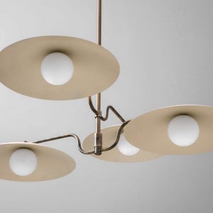 May include: A modern ceiling light fixture with four beige, disc-shaped shades. Each shade has a white, spherical light bulb in the center. The fixture has a bronze-colored metal frame and is suspended from the ceiling.