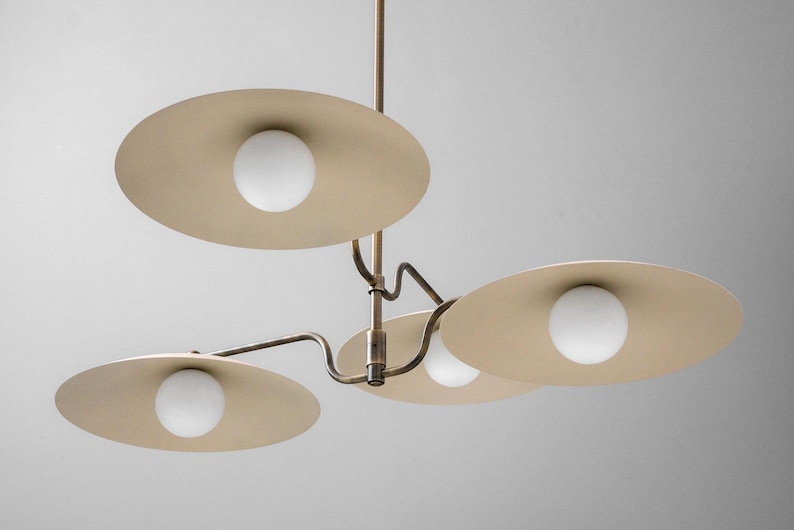 May include: A modern ceiling light fixture with four beige, disc-shaped shades. Each shade has a white, spherical light bulb in the center. The fixture has a bronze-colored metal frame and is suspended from the ceiling.