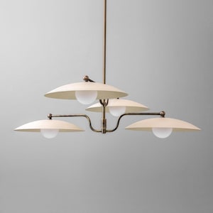 May include: A modern chandelier with a brass finish and four off-white, saucer-shaped shades. Each shade has a spherical, frosted glass light. The fixture hangs from a central rod.