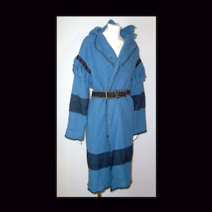 May include: A long, bright blue coat featuring a hood, dark blue horizontal stripes on the sleeves and lower body, and black whipstitch detailing along the edges. The coat includes fringe accents on the shoulders and a dark, textured belt with a buckle.