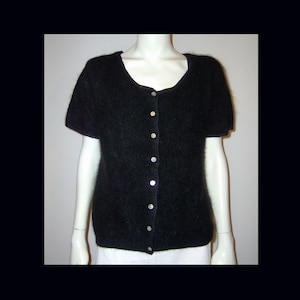 May include: A black, short-sleeved cardigan with a scoop neck and a row of silver buttons down the front. The soft, fuzzy texture of the sweater is visible. The garment is displayed on a white mannequin.