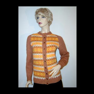 May include: A vintage brown cardigan with a geometric pattern in orange, yellow, and white. The long-sleeved sweater has a button-up front and is displayed on a mannequin. The sweater's design is reminiscent of the 1960s and 1970s.