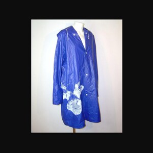 May include: A vibrant blue raincoat with a hood and white buttons. The coat features a white and gray abstract design on the lower front. The raincoat is displayed on a mannequin.