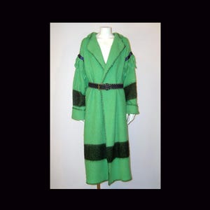May include: A long, bright green coat featuring dark green horizontal stripes on the sleeves and lower body. The coat includes fringe details on the shoulders, a dark belt at the waist, and visible dark stitching along the lapels and edges.