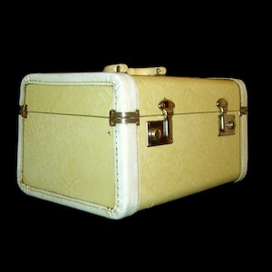 May include: A vintage off-white hard-sided suitcase with white trim and gold hardware. The suitcase has two latches and a handle.