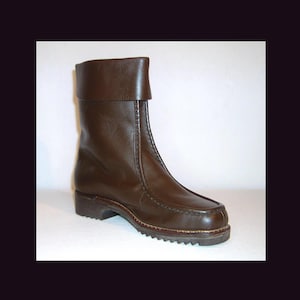 May include: A brown leather boot with a folded-over cuff. The boot features a rounded toe, a low heel, and a stitched sole. The boot is made of smooth, dark brown leather, and appears to be vintage.