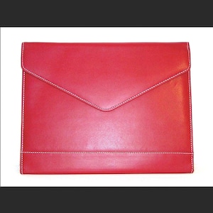 Puede incluir: Un bolso de mano de cuero rojo brillante con costuras blancas. El bolso tiene un cierre de solapa y una forma rectangular. Las costuras blancas son visibles a lo largo de los bordes y la solapa.