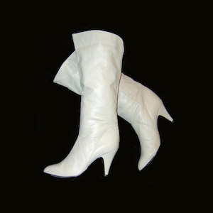 Puede incluir: Un par de botas altas de color crema con puntera y tacones de aguja. Las botas están hechas de un material liso y tienen una parte superior doblada. Los tacones miden aproximadamente 7.6 cm de alto.