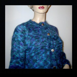 May include: A blue and purple knit cardigan with a round neckline and three large, gold-colored buttons. The textured knitwear has a fuzzy appearance. The garment is displayed on a mannequin.