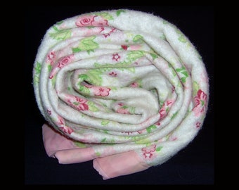 May include: A white fleece blanket with a pink floral pattern is rolled up. The blanket has a pink satin trim.