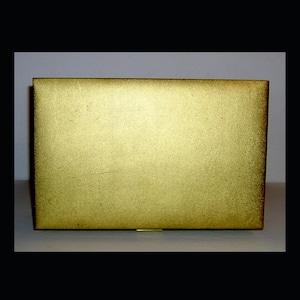 Może przedstawiać: Prostokątne, złote pudełko o teksturowanej powierzchni. Pudełko ma prosty, elegancki design i małe zapięcie. Ogólny wygląd sugeruje przedmiot vintage lub antyczny, prawdopodobnie pudełko na biżuterię lub drobiazgi.