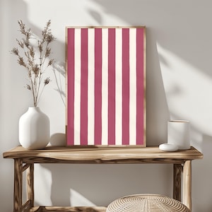 Może przedstawiać: Oprawione dzieło sztuki z pionowym wzorem w paski w odcieniach bordowego i kremowego. Grafika jest prezentowana na drewnianym stole konsolowym, obok białego wazonu z suszonymi kwiatami i małego białego ceramicznego pojemnika.