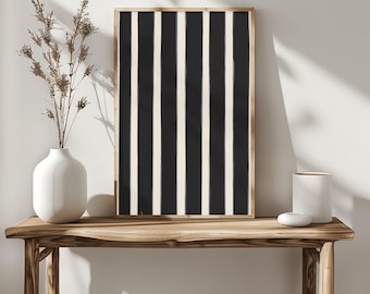 May include: A framed vertical art print with a black and off-white striped pattern. The artwork is displayed on a wooden console table, alongside a white vase with dried flowers and other decorative items. The overall aesthetic is minimalist and modern.