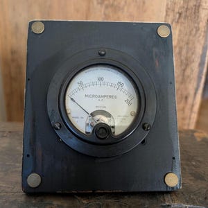 Può includere: Un vecchio misuratore di microampere AC Weston Modello 30. Il misuratore è alloggiato in una cornice quadrata di legno nero con accenti angolari color ottone. L'indicatore circolare mostra un quadrante bianco con segni neri e un ago.