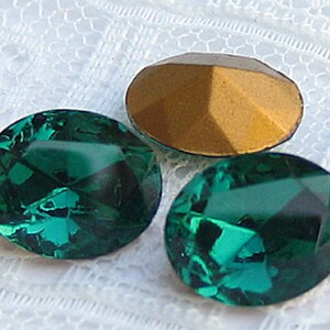 May include: Three oval-shaped, faceted, green glass rhinestones. The rhinestones are on a white lace background.