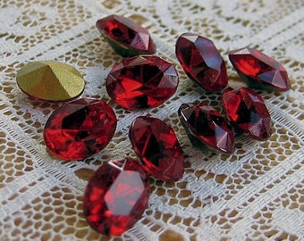 May include: A collection of ten red oval-shaped rhinestones on a white lace background.