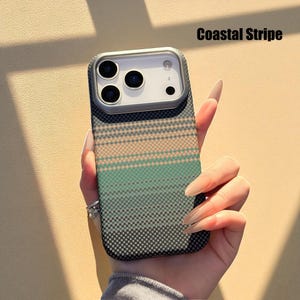 May include: A phone case with a Coastal Stripe design. The case features a pattern of horizontal stripes in shades of green, peach, and gray. The case has a camera cutout and is held by a person.
