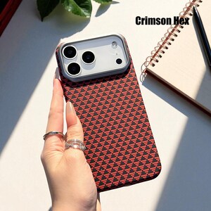 May include: A phone case with a red and black geometric pattern. The case has a clear camera lens protector and the text "Crimson Hex" is visible. The phone case is held by a person.