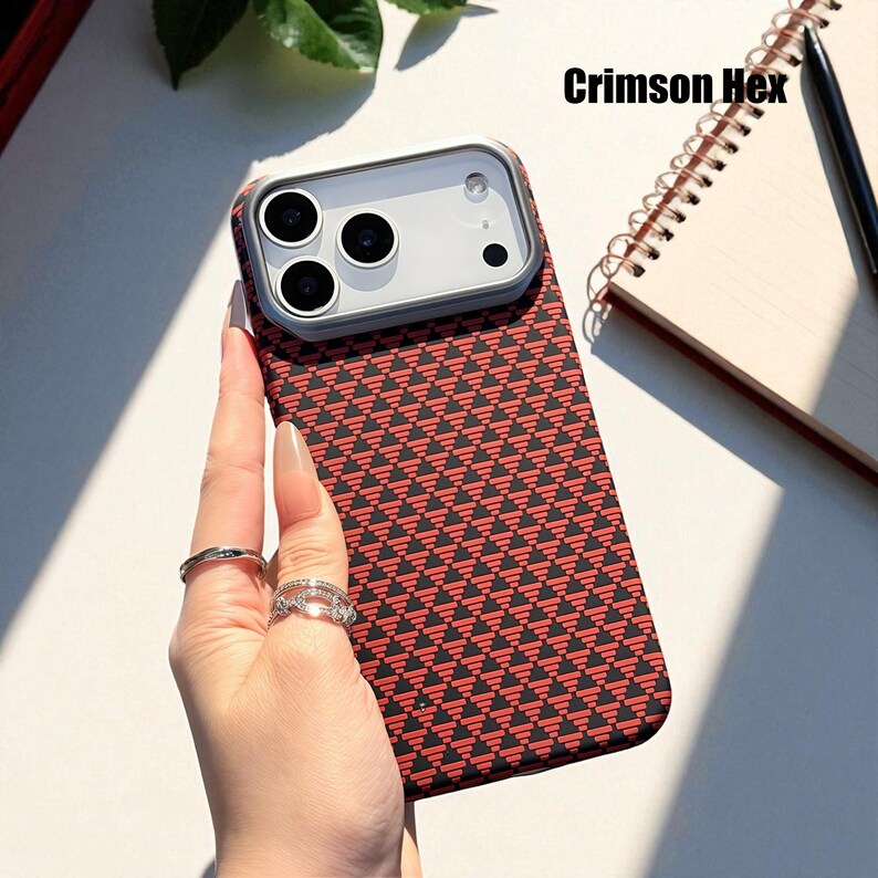 May include: A phone case with a red and black geometric pattern. The case has a clear camera lens protector and the text "Crimson Hex" is visible. The phone case is held by a person.