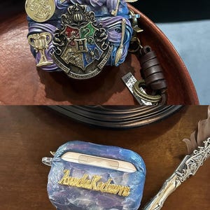 May include: Two Airpod cases. One is a blue and purple case with a galaxy design and the text "Avada Kedavra" in gold. The other is a purple and blue case with the Hogwarts crest and the text "Hogwarts" in gold.