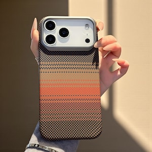 May include: A mobile phone case featuring a geometric design in brown, orange, and black. The case incorporates a camera module with three lenses and a flash. The case is held by a person.