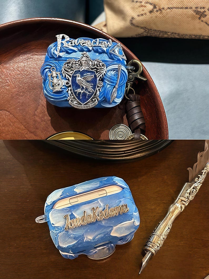 May include: Two blue and silver Airpod cases with different designs. One case features the Ravenclaw house crest with the words "Ravenclaw" in silver lettering. The other case has a blue and white marbled design with the words "Avada Kedavra" in silver lettering.