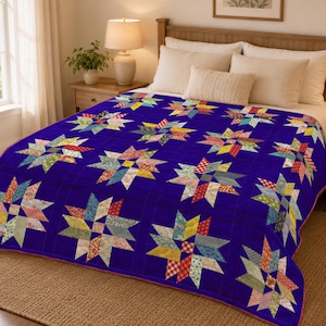 May include: A quilt featuring a deep blue background with a repeating pattern of multi-colored star blocks. Each star is constructed from various fabric scraps in shades of red, yellow, green, and blue, creating a vibrant contrast against the solid blue field.