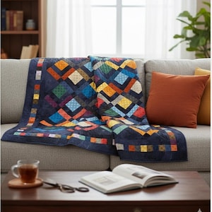 Puede incluir: Una colcha colorida con un patrón geométrico, sobre un sofá gris. La colcha presenta cuadrados y rectángulos en tonos azules, naranjas, amarillos y verdes. Una almohada naranja descansa en el sofá. Una taza de té y un libro abierto están en la mesa de centro.