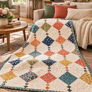 Könnte beinhalten: Ein Steppdecke mit einem sich wiederholenden Rautenmuster auf cremefarbenem Hintergrund. Die Rauten sind mit kleinen Blumenmustern in Marineblau, Senfgelb, Olivgrün und Korallenorange gefüllt und durch winzige quadratische Akzente verbunden.