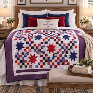May include: A quilt featuring a patchwork design of red, white, and blue squares with large red and blue star appliques. The quilt has a purple border and is draped over a bed with white, navy blue, and red pillows, including one with the text Home Sweet Home.