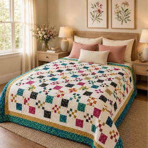 May include: A patchwork quilt featuring a repeating block pattern in white, teal, magenta, black, and yellow. The quilt has a wide teal border with a floral print and a thin yellow inner border, covering a bed with pink and cream pillows.